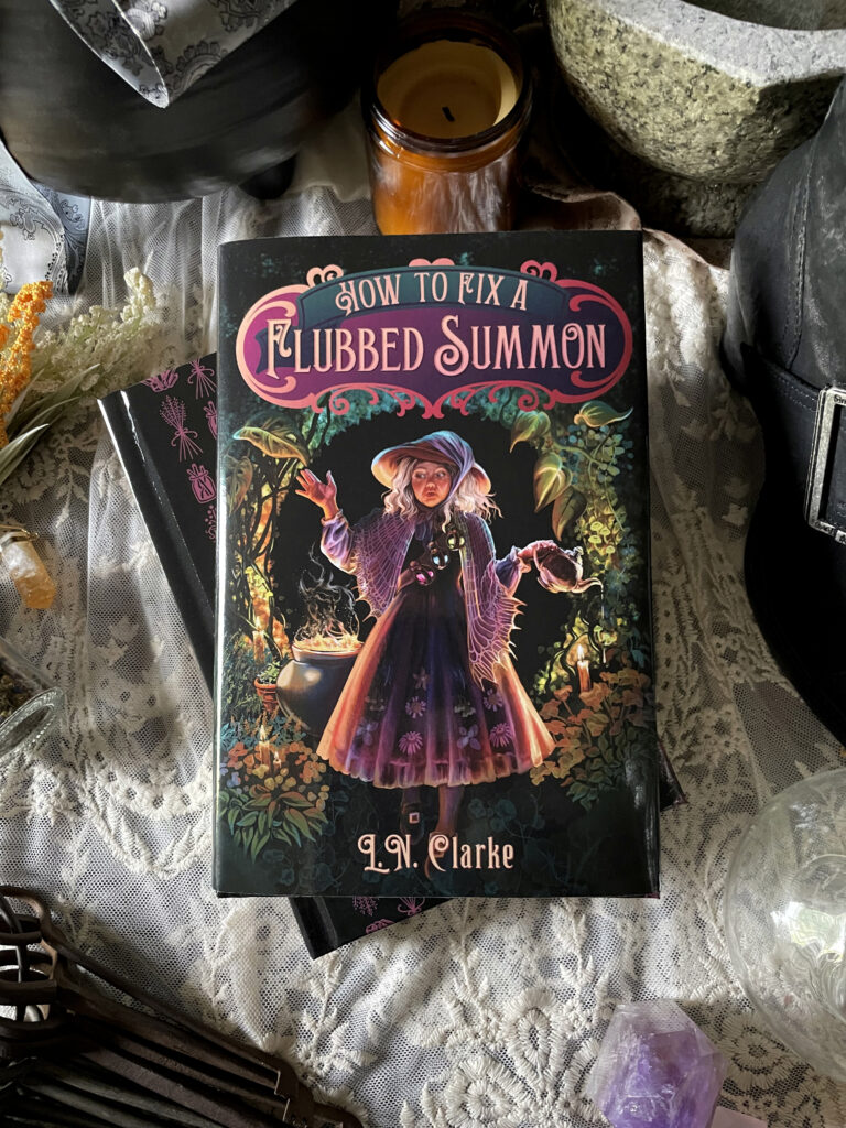 Photograph of the hardcover book "How to Fix a Flubbed Summon" amidst small objects such as keys, candles, flowers, and crystals.